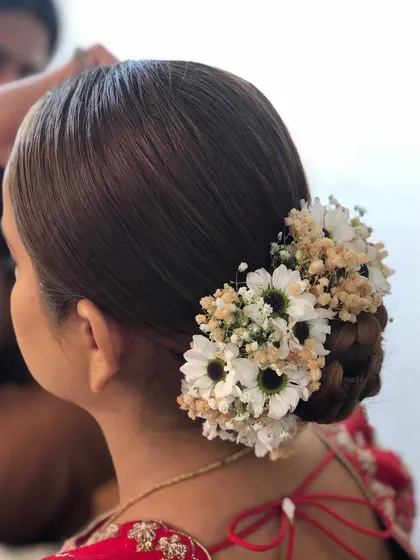 A close-up of a braided bun adorned with a mix of daisies and baby's breath. The braided texture adds a lovely detail to the classic floral bun style.