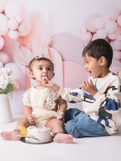 Sharing is caring! An older brother sweetly offers his baby sister a taste of her first birthday cake.