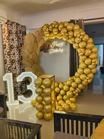 An elegant and trendy setup for a 13th birthday celebration at home. I used a circular balloon arch made of monochrome gold balloons, accented with dried pampas leaves and a large '13' marquee light.