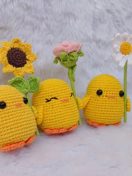 Three of my crochet ducks, each holding a different flower: a sunflower, a rose, and a daisy. They have different expressions for added personality.