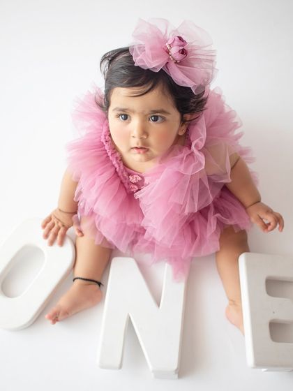 An adorable overhead shot for a first birthday, with the baby girl sitting among giant "ONE" letters in a fluffy pink dress.