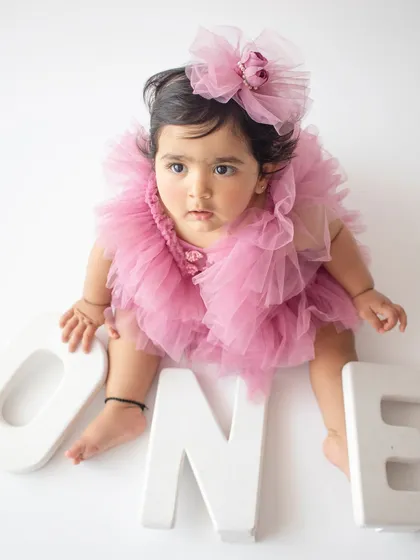 A birthday girl in a fluffy pink tulle dress poses with "ONE" letters against a clean white background.