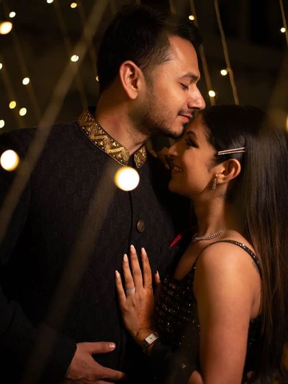 A tender forehead kiss amidst twinkling fairy lights. This is a classic pre-wedding shot that captures the warmth and intimacy of your relationship.