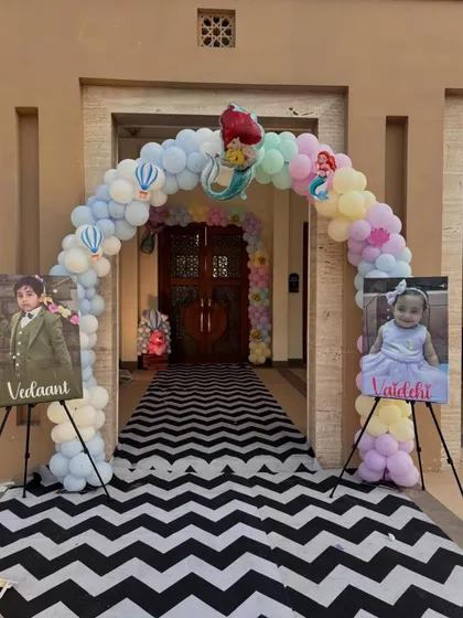 A grand entrance for a twins' birthday party, showcasing a combined theme. The pastel balloon arch welcomes guests, while personalized photo easels for each child stand on either side.