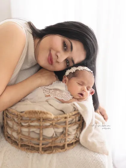 A mother's gentle love. She rests her head near her sleeping newborn, who is nestled safely in a rustic basket. A portrait of peace and deep affection.