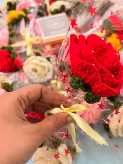 A close-up of a single, vibrant red crochet rose. The detailed petals and green leaves make it look just like the real thing.