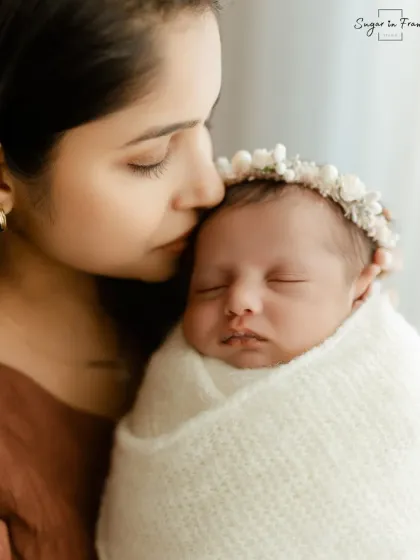 A close-up portrait of a mother gently kissing her sleeping newborn's head. A simple, beautiful expression of a mother's love.