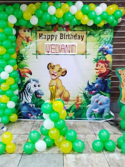 A jungle-themed birthday decoration with a Lion King backdrop and a green and yellow balloon arch. This is a classic and popular theme for a first birthday.