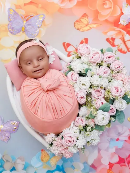 A beautiful smiling newborn in a heart-shaped bowl, surrounded by a rainbow of flowers and butterflies. This is pure joy.