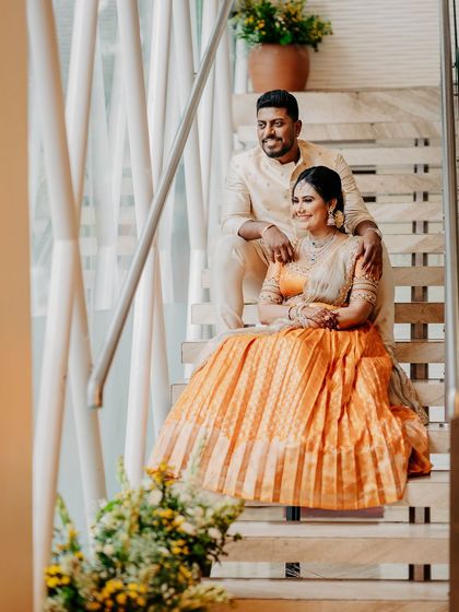 A full-length shot of the couple on the stairs, showcasing the beautiful pleated skirt of her half saree and his elegant kurta set.