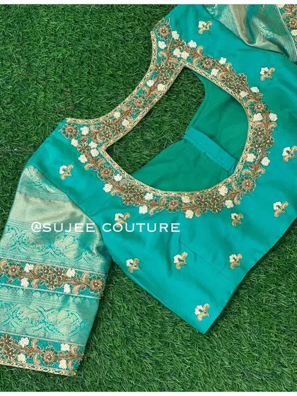 A beautiful teal blouse with contrasting light green Kanchipuram silk sleeves. The square back neckline is adorned with delicate floral and zardozi embroidery.