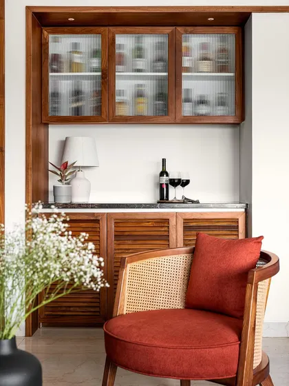 This compact bar unit features a marble countertop, louvered wooden shutters on the bottom, and fluted glass cabinets on top, creating a classic and functional piece.