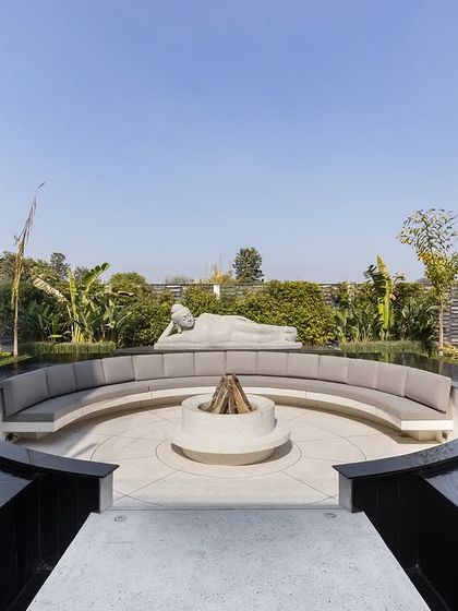 This circular fire pit and seating area, surrounded by water, is designed for heartwarming moments. The space is anchored by a reclining Buddha statue, creating a focal point for gathering and connection in a tranquil, open-air setting.