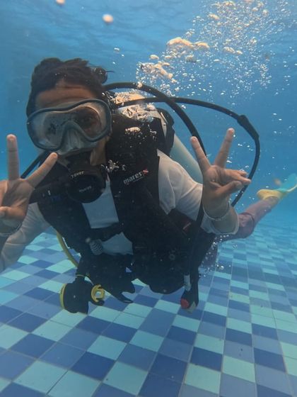 Double peace signs from an enthusiastic participant during a pool-based scuba training session.