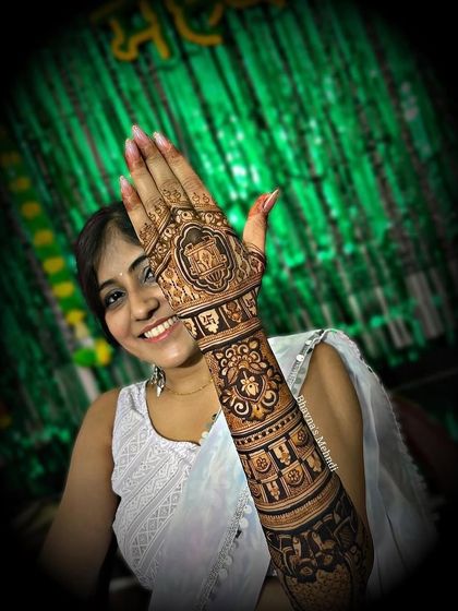 A smiling bride showing off her full arm mehndi. The design is a beautiful example of traditional bridal art, rich in detail and symbolism.