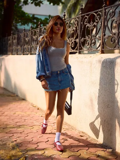 A full street-style look featuring the red studded ballet flats. The model’s confident stride shows that these shoes are made for walking, blending high fashion with real-world function.