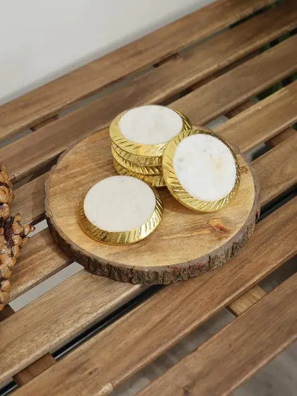 These round marble coasters feature a textured gold rim, adding a touch of classic elegance to any setting. They are displayed here on a rustic wooden slice, showcasing their versatility.