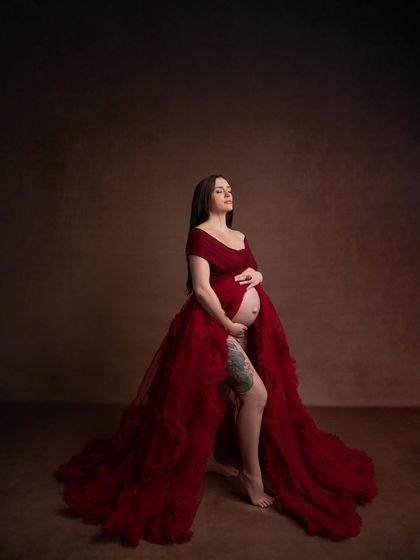A powerful stance in the red gown, exuding confidence and grace. This image celebrates the strength and beauty of the female body during pregnancy.