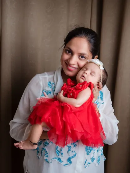 A mother's gentle hold and a sleeping baby in a vibrant red dress make for a stunning portrait. We love capturing the special connection between a mom and her newborn.