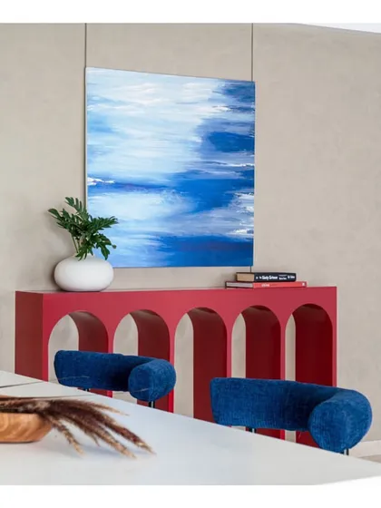 A pop of color and modern art defines this corner. The vibrant red console table with its repeating arches makes a bold statement, beautifully complemented by the abstract blue painting.