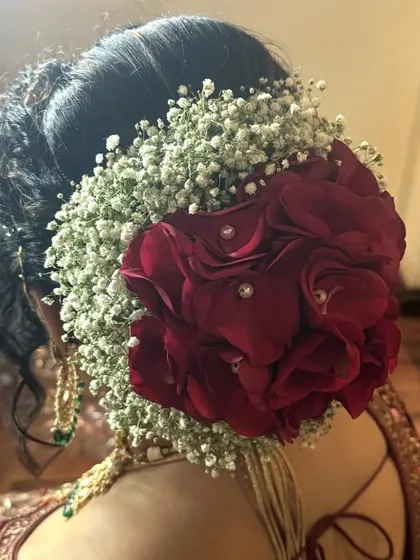 A classic bridal bun adorned with a halo of baby's breath and a large red rose. This is a timeless and romantic choice for any traditional wedding ceremony.