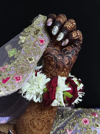 A close-up of the bride's hand, showing the detail of the henna stain against her embroidered sleeve.