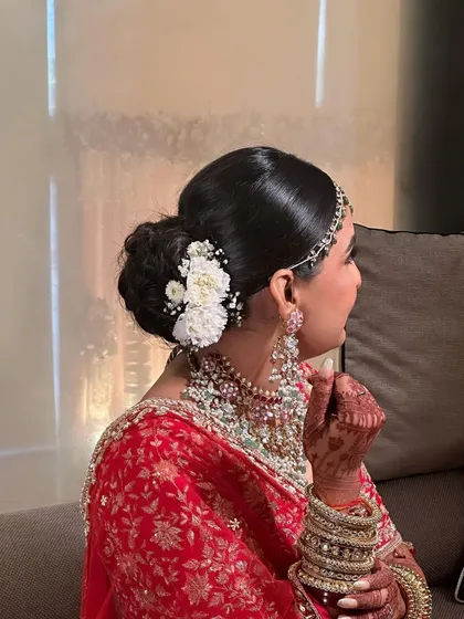 This classic bridal bun is adorned with fresh white carnations and baby's breath. It's a timeless choice that perfectly complements a traditional red lehenga for the Pheras.
