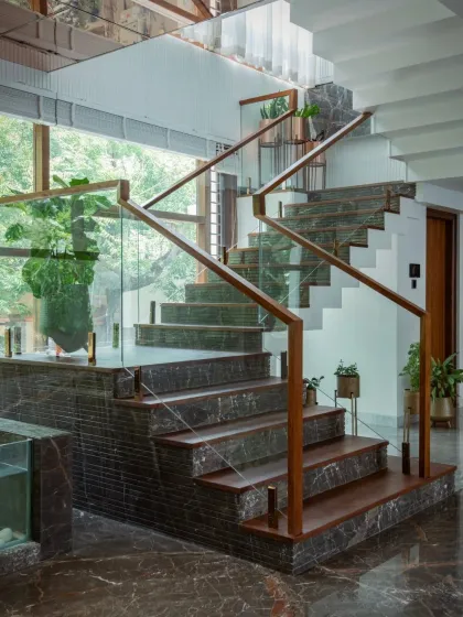 Views of the staircase adjacent to the pooja room, showing the combination of dark marble, wood treads, and glass railings that create a warm yet modern aesthetic.