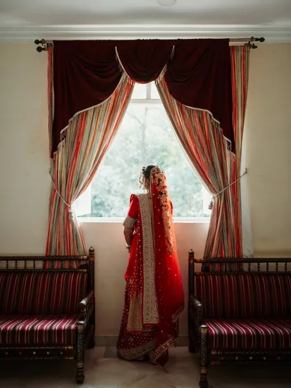 An artistic shot of the bride from behind, looking out a window, showcasing the beautiful details of her saree and hairstyle.