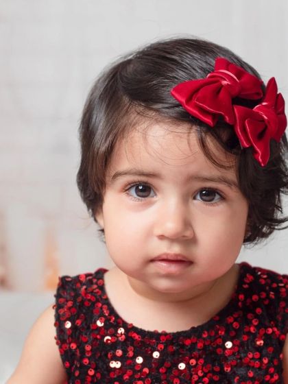 A beautiful close-up portrait of a baby girl, where her expressive eyes and the festive red bow are the stars of the shot.