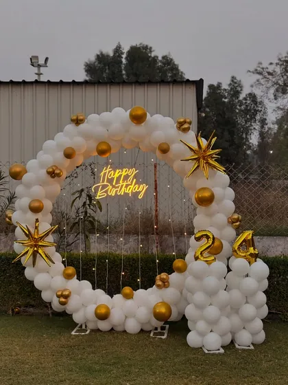 An elegant outdoor balloon ring in all white with gold accents, perfect for a 24th birthday celebration in a garden or farmhouse.