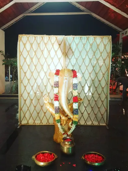 A simple and respectful setup for a puja. A Ganesha idol is placed before a clean, elegant backdrop, with a traditional garland and bowls of fresh flower petals for offerings.