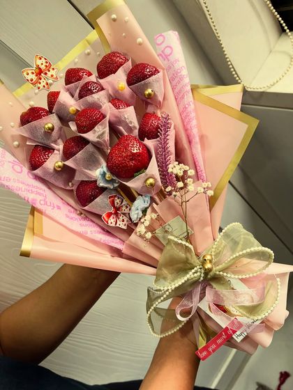 Two hands hold this lovely pink-wrapped strawberry bouquet, showing its generous size. It's a gift meant to be shared, or enjoyed all by yourself.