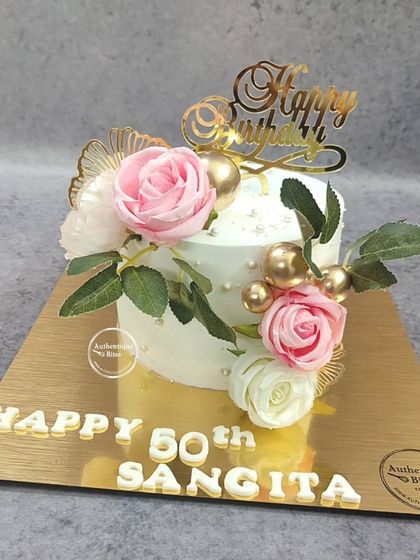 A beautiful 50th birthday cake decorated with pink and white roses, gold spheres, and a golden "Happy Birthday" topper.