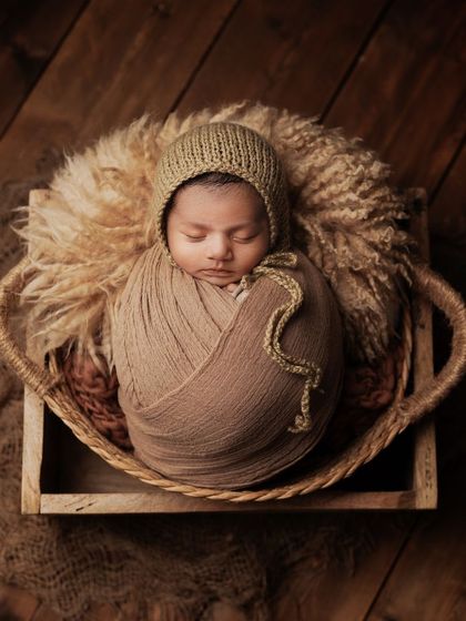 A tiny miracle nestled in a basket. This overhead shot showcases the beautiful textures of the brown wrap, bonnet, and the fluffy wool layer inside the basket.