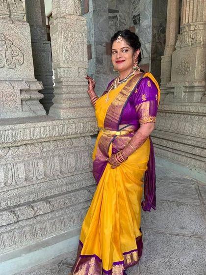 A full-length shot of Pratima at a temple, showing her complete traditional look with a beautiful yellow and purple silk saree.
