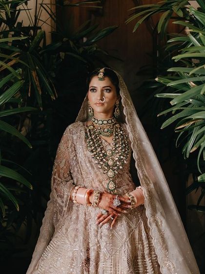 A stunning portrait of Megha framed by lush green foliage. The contrast between the natural environment and her ornate bridal attire creates a visually striking and beautiful image.