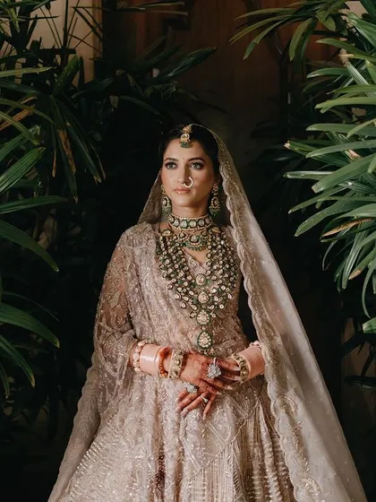 A stunning portrait of Megha framed by lush green foliage. The contrast between the natural environment and her ornate bridal attire creates a visually striking and beautiful image.