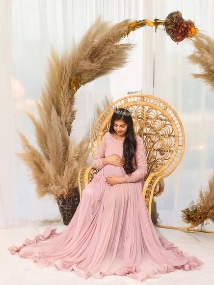 A beautiful solo portrait in a boho-themed studio setting. The mother-to-be is seated on a peacock chair, framed by an arch of pampas grass, creating a warm and trendy look.
