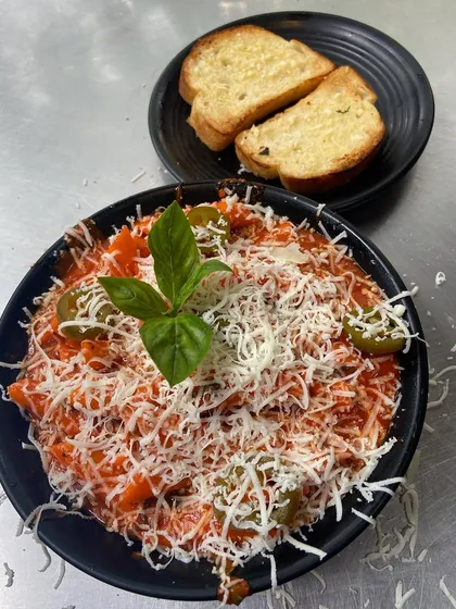 My Arrabbiata Pasta is a spicy and tangy delight, topped with cheese and fresh basil, and served with garlic bread.