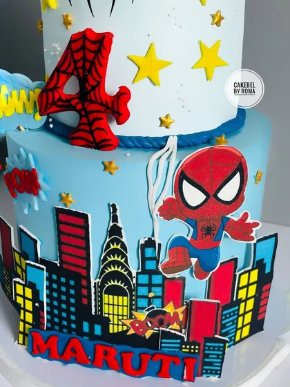 A close-up of the bottom tier of the two-tier Spider-Man cake, showing the detailed city skyline and the chibi-style Spidey swinging by.