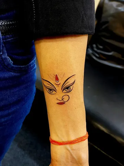 The powerful eyes of the Goddess Durga, captured in a minimalist design. With a simple red bindi for contrast, this tattoo is a subtle yet strong symbol of divine feminine power.