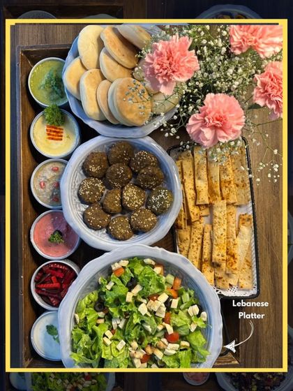 Our Lebanese Platter, beautifully arranged for gifting or serving at a party. It features a complete spread of falafel, pita, various dips, and salad, adorned with fresh carnations.