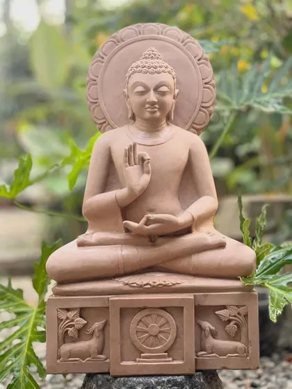 This serene Gautama Buddha statue, hand-carved from pink sandstone, is shown in the dharmachakra pravartana mudrā, or the teaching posture. It is a perfect sculpture for creating a peaceful atmosphere in any indoor or garden space.