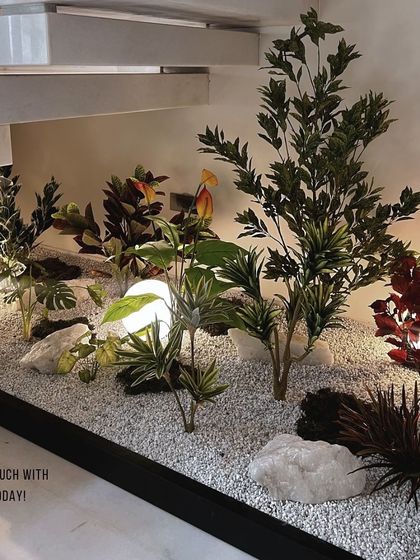 This angle highlights the thoughtful placement of varied faux plants and decorative rocks within the under-staircase garden. The composition feels balanced and natural, offering visual interest from every viewpoint.