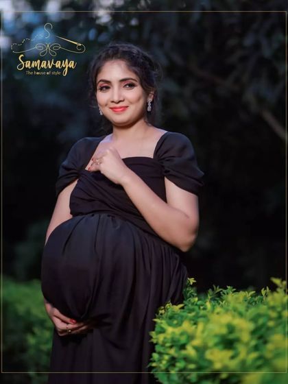 A three-quarters portrait in a lush green setting, the black gown providing a beautiful contrast and highlighting the baby bump.