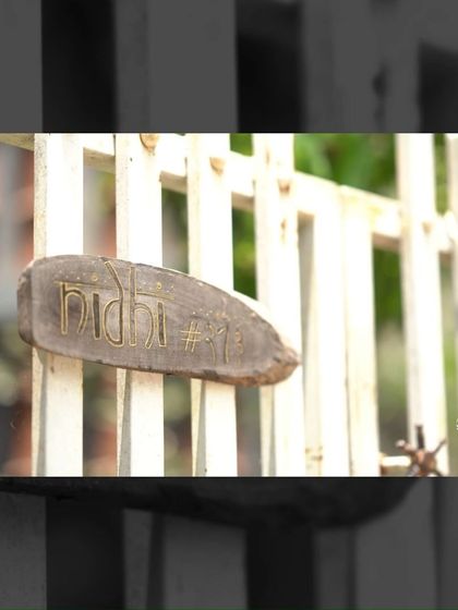 The home's name, 'Nidhi', is carved into a rustic piece of wood at the entrance gate, offering a personal and handcrafted welcome.