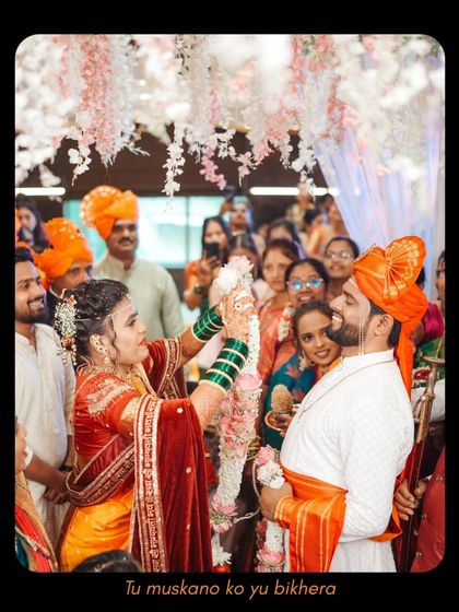 The bride joyfully places the garland on the groom, surrounded by smiling family and friends. This candid shot captures the festive atmosphere and collective happiness of the wedding ceremony.