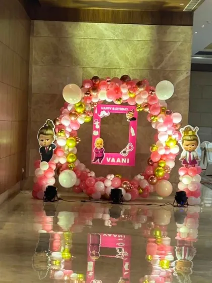 A circular balloon photo booth for a "Boss Baby" themed party, using pink, white, and gold balloons with a personalized frame in the center.