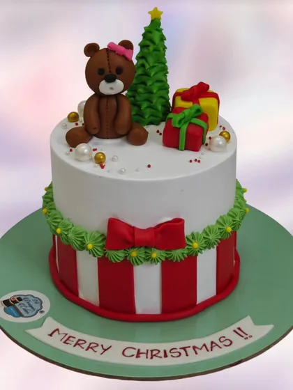 A festive Merry Christmas cake with a teddy bear, a Christmas tree, and presents. A sweet centerpiece for a holiday celebration.